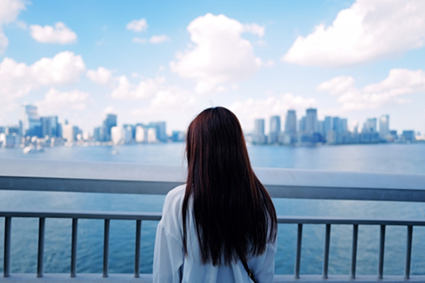 海辺の手すり越しに都市の街並みを眺める女性